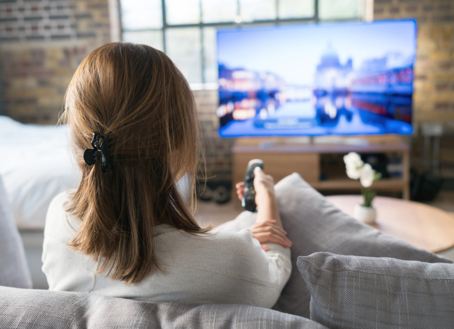 Woman relaxing at home watching tv and holding the remote control