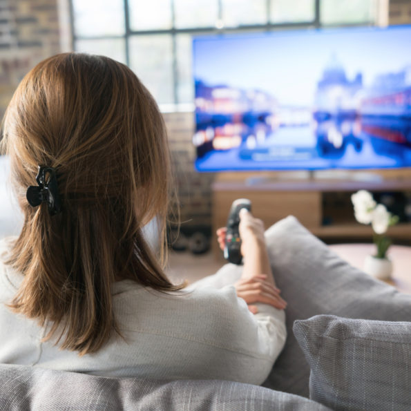 Woman relaxing at home watching tv and holding the remote control